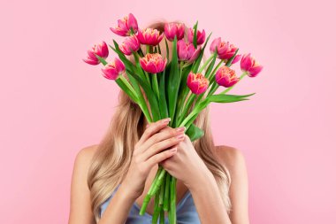 Özel durumlar için çiçekler. İsimsiz genç bir bayan pembe stüdyo arka planında yüzüne bir buket lale tutuyor. Romantik milenyum bağı bayramı kutluyor.