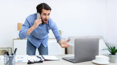 Kızgın iş adamı telefonda dizüstü bilgisayara bakıyor, ofiste bilgisayar sorunu yaşıyor. İletişim, Dünya Sorunları ve Çatışmalar Konsepti. Panorama, Seçici Odaklanma