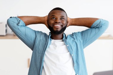 İçişleri Bakanlığı 'nda sandalyeye yaslanan, işyerinde dinlenen, pozitif Siyah Erkek Serbest Çalışan. Hayalperest Afrikalı Adam başarılı bir işten sonra ellerini başının arkasına koyup dizüstü bilgisayarla masada oturuyor.