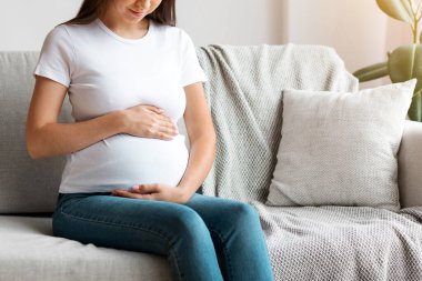 Portrait Of Young Beautiful Expectant Lady Relaxing On Comfortable Couch In Living Room, Smiling Beautiful Millennial Pregnant Woman Tenderly Touching Her Belly, Enjoying Prenatal Time, Free Space