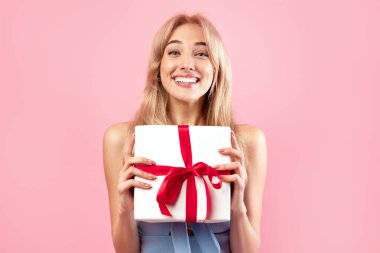 Bahar tatili kutlaması. Güzel elbiseli neşeli bin yıllık bayan, kadınlar günü için hediye paketi ya da pembe arka planda doğum günü kutusunu gösteriyor. Genç sarışın özel bir sürprizle mutlu oluyor.