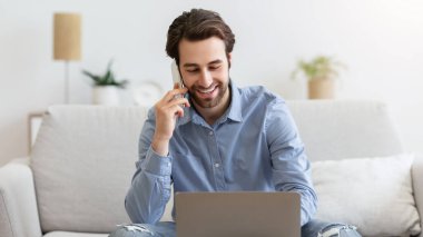 İş konuşması. Cep telefonuyla konuşan, bilgisayarını kullanan evden uzakta çalışan, koltukta oturan bir adam. Freelancer bilgisayarda çalışırken telefonla konuşuyor. Serbest ve Mesafeli Çalışma Konsepti