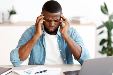Baş ağrısı konsepti. İş yerinde migren ağrısı çeken stresli siyahi adam, dizüstü bilgisayarla masada oturan ve şakaklarına dokunan yorgun Afrikalı Amerikalı adam, güçlü bir ağrı ya da kan basıncı, boş alan...
