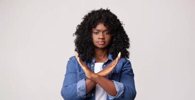 Gri stüdyo arkaplanı üzerinde dur işareti gösteren sinirli genç siyahi kadın, fotokopi uzayı. Afrikalı kıvırcık kadın ırkçılığı, cinsiyetçiliği, şiddeti, tacizi protesto ediyor.