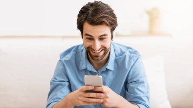 Evdeki koltukta oturan ve kulaklık takan cep telefonuyla video görüşmesi yapan mutlu adam. Modern Uzaktan İletişim. Teknoloji ve Gadget, Mobil Uygulama Konsepti