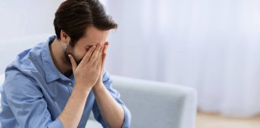 Erkek Depresyonu. Evdeki koltukta oturan sinirli, ağlayan ve yüzünü kapatan adam. Çaresiz adam oturma odasında ağlıyor. Mutsuzluk ve stresli modern hayat kavramı. Metin için Boşluk