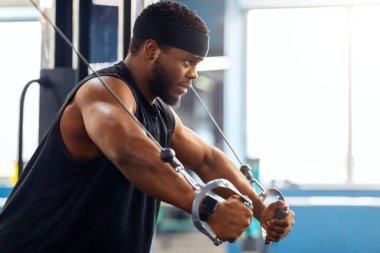 Spor salonunda trisepsleri çalıştıran genç siyah sporcu, fotokopi alanına bakıyor. Motive edilmiş Afro-Amerikan vücut geliştirici modern spor salonunda çalışıyor, çapraz makine kullanıyor.