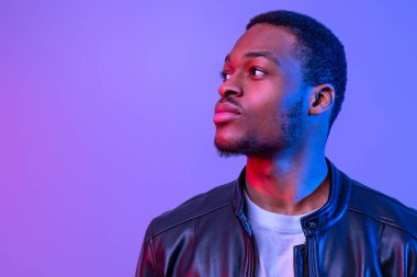 Tarz sahibi deri ceketli yakışıklı Afrikalı genç adam diğer tarafa bakıyor, Mor Arkaplanda Neon Işığı Altında duran çekici siyahi adam,