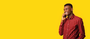 Mobil İletişim. Pozitif Afrikalı Amerikalı Cep telefonuyla konuşan ve kafasını çeviren genç siyah adam, sarı arka planda tek başına dururken keyifli sohbetin tadını çıkarıyor, Boşluğu Kopyala