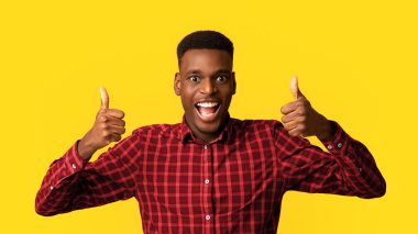 Her şey harika. Neşeli afro-amerikan adam başparmağını kaldırıyor, iki eliyle onay jesti yapıyor ve kameraya gülümsüyor, sarı stüdyo arka planında tek başına duruyor, boş alana yakın duruyor.