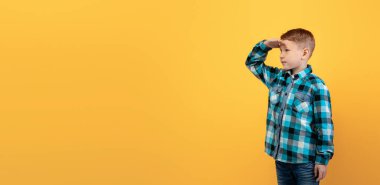 Alnının yanında flanel tutan tatlı kızıl çocuk fotokopi odası, panorama, sarı stüdyo arka planı. Meraklı kızıl saçlı çocuk çocuklar için heyecan verici bir reklam izliyor.