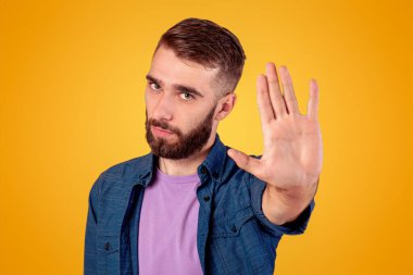 Ciddi hippi adam, gri stüdyonun arka planında kameraya el hareketi yapıyor. Genç adam olumsuz tutumunu ifade ediyor, bir şeyi reddediyor ya da yasaklıyor.