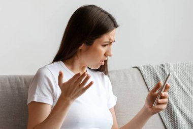 Stresli hamile kadın koltukta dinlenirken akıllı telefon ekranına bakıyor, endişeli bayan cep telefonunda nahoş mesajlar okuyor, kötü haberlere duygusal tepki veriyor, boş alan arıyor.