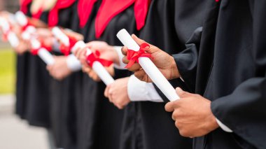 Siyahlar ve kırmızılar içinde mezuniyet kostümleri içinde üniversite kampüsünde açık havada mezuniyet töreni sırasında sırada bekleyen diplomaları olan uluslararası bir grup.