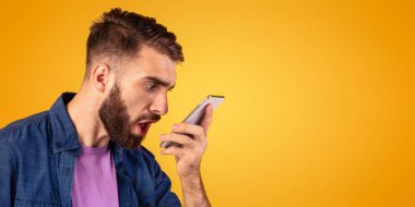 Kızgın sakallı adam akıllı telefona portakal rengi stüdyo arka planında bağırıyor, panorama. Memnun olmayan müşteri cep telefonuyla çatışmaya giriyor. Stres yönetimi ve olumsuz duygular kavramı