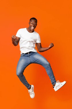 Havaya atlayıp komik figürler gösteren, güzel bir gün geçiren, turuncu arka planda olumlu duygular gösteren sevimli siyahi adam. Afrikalı Amerikalı stüdyoda poz veriyor, eğleniyor.
