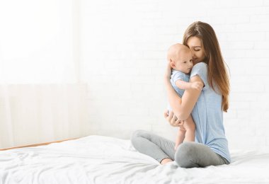 Koşulsuz sevgi. Yeni doğmuş bebeğiyle bağ kuran genç bir kadının portresi, evde yatakta oturuyor, boş bir alan.