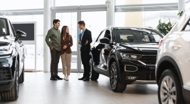 Araba almak ya da kiralamak. Bayilikte, panoramada yeni bir otomobil almak için pazarlamacıyla konuşan pozitif genç eşler. Başarılı milenyum yöneticisi, müşterilere kuaförde araç seçimi gösteriyor