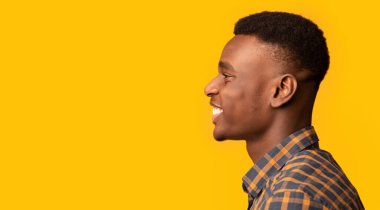 Fotokopi uzayına yan bakan neşeli Afrikalı Amerikalı adamın profil fotoğrafı, damalı gömlekli adamın sarı arka planda, Panorama 'da tek başına duruşu.