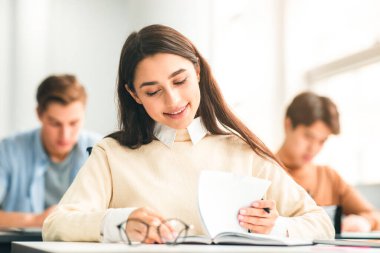 Kampüste Yeni Yıl. Modern sınıftaki masada oturan, test egzersizi yapan, ders okuyan, eğitimin keyfini çıkaran ve öğrenmenin tadını çıkaran pozitif, genç ve güzel bir bayan.