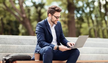 Şehir parkında, panoramada merdivenlerde otururken dizüstü bilgisayarla çalışan mutlu girişimci