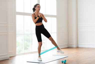 Vücut Şekillendirme Konsepti. Siyah Spor Giyim Giyimi Giyen, Yoga minderi üzerinde duran, Kablosuz Kulaklık takan, Müzik eşliğinde Pencereye Yakın Antrenman yapan,