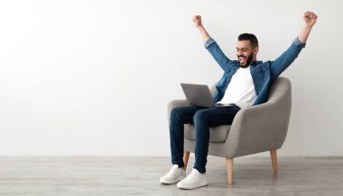 Bin yıllık Arap bir adam dizüstü bilgisayarla koltukta oturup online galibiyeti kutluyor ya da beyaz stüdyo duvarına karşı başarısını kopyalıyor. Doğu 'lu genç adam web mağazasında büyük indirimin keyfini çıkarıyor.