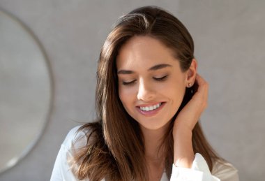 Evdeki banyoda doğal makyajlı utangaç güzel bir kadının portresi kusursuz cildine bakan, saçlarına dokunan, fotokopi çeken, yakın çekim yapan bir kadın.