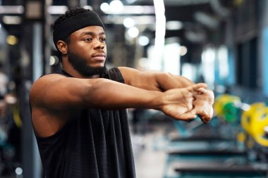Spor salonunda ellerini ve parmaklarını uzatıp fotokopi odasına bakan atletik siyahi bir adam. Kas yığını Afro-Amerikan sakallı sporcu antrenmandan önce ısınıyor. Etkin yaşam tarzı kavramı