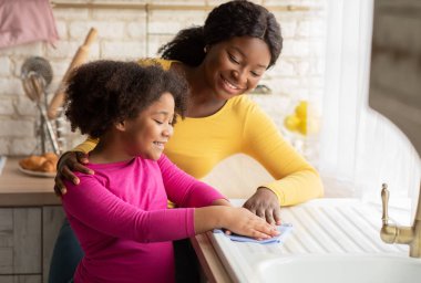 Kara Anne 'yi Sevmek, Kızına Ev Bakımı, Temizlik Mutfağı Birlikte Öğretmek. Sevimli küçük kız bezle masayı siliyor ve gülümsüyor, ev işlerine yardım ediyor, boş alan arıyor.