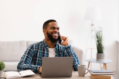 Gülümseyen siyahi iş adamı telefonda konuşuyor modern ofiste işyerinde oturuyor. Mobil İş İletişim ve Girişimcilik. İş yerinde cep telefonu sohbeti yapan adam.