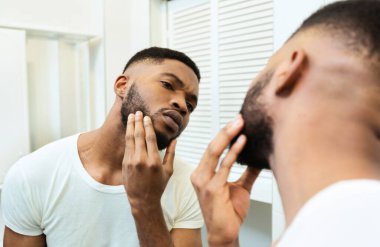 Tıraş olmam lazım. Konsantre olmuş Afrikalı adam banyo aynasına sakalına bakıyor.