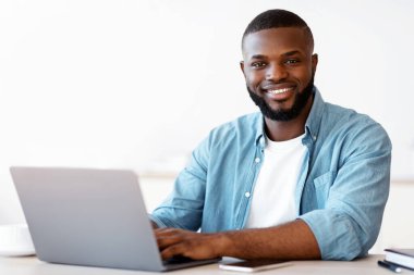 Başarılı Siyah Serbest Çalışan Adam 'ın portresi, bilgisayarla masada poz veren, kamerada gülümseyen Afro-Amerikan adam, İçişleri Bakanlığı' nda bilgisayar üzerinde çalışırken, ücretsiz alan