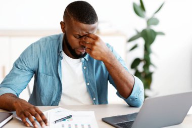 Ofisteki stresli siyahi iş adamının portresi, depresif Afrikalı Afrikalı Amerikalı girişimci masada dizüstü bilgisayar ve belgelerle oturuyor, iş yerinde sorunlar yaşıyor,