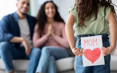 Anneler Günü Hediyesi. Sevimli küçük kız, annesini seven, hediyesini arkasında tutan, annesini tatille tebrik eden ve seçici bir şekilde odaklanan annesine kocaman kırmızı bir kalp çizerek tebrik kartı hazırla.