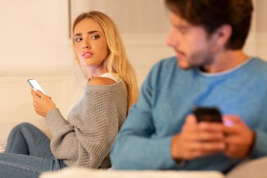 Hile ve sadakatsizlik. Kocası Evde Kanepede Şüpheli Karısı Yanında Oturan Cep Telefonu Mesajlaşma. Seçici Odak