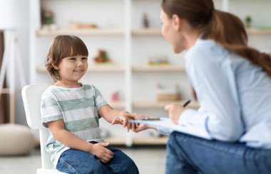 Hastayla ilk görüşme. Arkadaş canlısı profesyonel kadın çocuk psikoloğu küçük sevimli çocuğu selamlıyor, eline dokunuyor ve ofiste gülümsüyor.