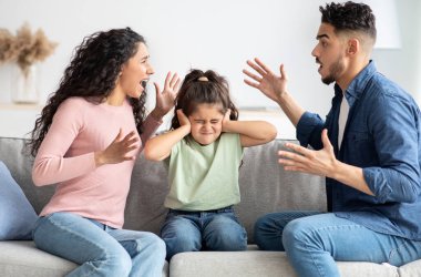 Parental Quarrels. Arab Man And Woman Arguing In Front Of Their Child, Upset Little Girl Covering Ears With Hands Not To Listen Conflict, Stressed Female Kid Sitting Between Shouting Parents