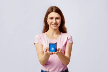 Atık Ayrım Konsepti. Kağıt çöpleri için küçük mavi oyuncak kutusunu tutan gülümseyen genç bir kadının portresi, çöp geri dönüşümünü teşvik eden, açık gri arka planda ayakta duran bir kadın.