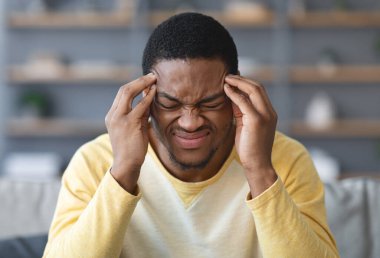Evinde baş ağrısı çeken, şakaklarına dokunan, fotokopi çeken, geçmişi bulanık genç Afrikalı Amerikalı adama yakın çekim. Migren, baş ağrısı, stres, gerilim sorunu, akşamdan kalma konsepti