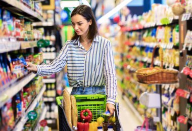 Süpermarkette. Markette koridorlar arasında Tramvay 'la duran genç kadının portresi. Keyifli Tüketiciler Yerel Dükkandan Temelleri Alırlar, Raflardan Ürünler Alırlar