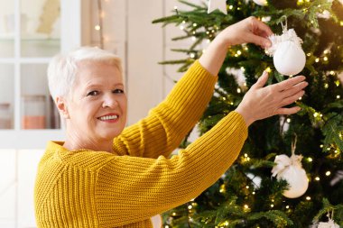 Gülümseyen yaşlı kadın Noel ağacını süslüyor. Mutfak içi, kopyalama alanı. Kış tatilinden önce Noel süslemeleri yapan kısa saçlı güzel yaşlı kadın aile partisine hazırlanıyor.