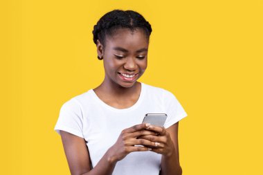 Neşeli Siyah Kadın Telefon Mesajlaşması ve Ağ Ağı Sarı Stüdyo Arkaplanının Üzerinde Duruyor. Akıllı telefonda cep telefonu kullanan Afrikalı genç bir bayan. Metin için Boşluk