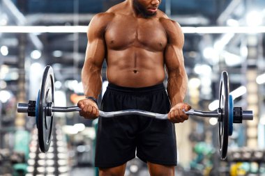 Atletik siyah adam ağırlık kaldırıyor ya da ağırlık kaldırıyor, ağır halterli ve göğüs kasları üzerinde çalışıyor, spor salonu içi. Kaslı üstsüz Afrikalı Amerikan vücut geliştirici, kopyalama alanı