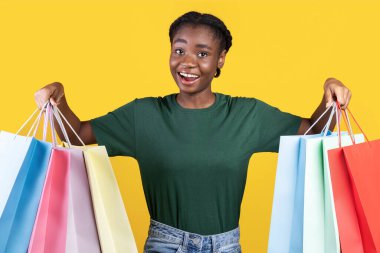 Renkli alışveriş torbalarıyla alışveriş pozu veren neşeli bayan alıcı sarı stüdyonun arka planında duruyor, kameraya gülümsüyor. Mevsimlik satışlar, indirimler, moda ve alışveriş. Mutlu Müşteri Konsepti
