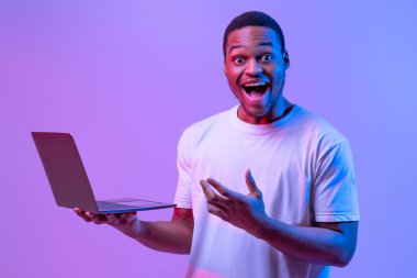 Güzel web sitesi. Heyecanlı Siyah Adam 'ın portresi, dizüstü bilgisayarı Neon Işıklandırma Altında, aşırı mutlu Afrikalı Amerikalı Adam laptopla başarıyı kutluyor, Mor Stüdyo Arkaplanı' nın başında duruyor,