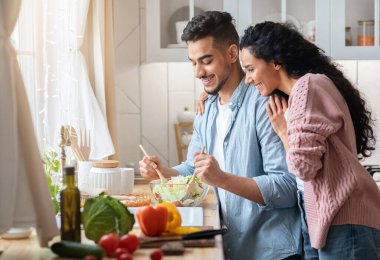 Birlikte yemek pişirmek. Mutlu Milenyum Orta Doğulu çift mutfakta yemek hazırlıyor, gülümseyen genç Arap eşler öğle yemeği için taze sebze salatası yapıyor, sağlıklı ev yemekleri yiyor, bedava yer açıyor.