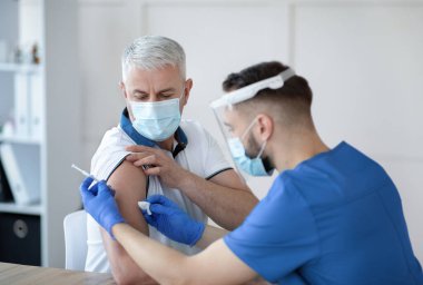 Genç doktor, hastanedeki yaşlı erkek hastaya koronavirüs aşısı yapıyor. Klinikte kovid 19 'a karşı bağışıklık kazanmış yetişkin bir adam. Küresel virüs salgınına karşı tıbbi tedavi