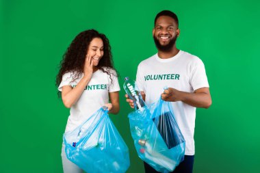 Bir çift çok kültürlü gönüllü plastik leke ve torba içinde şişe toplayarak yeşil stüdyonun arka planında dikilip kameraya gülümsüyor. Gönüllü Çalışma ve Ekoloji Konsepti