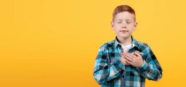 Gözleri kapalı, sarı stüdyo arka planında iki elini göğsüne koyan, dua eden ya da müteşekkir hisseden, içi boş bir panorama olan sevimli kızıl çocuk. Avuç içleri dolu barışçıl bir çocuk.